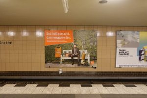 In einem Berliner U-Bahnhof eine Plakatwerbung der BSR zur Stadtsauberkeit aus 2021. Auf dem Plakat sitzt ein Geschäftsmann mit seinem Smartphone auf einer Bank, neben ihm seine Bürotasche. Neben der Bank steht ein Papierkorb mit der Aufschrift "Müllkippchen". Vor ihm liegt seine überdimensional große ausgedrückte Kippe. Die Headline der Kampagne lautet: „Erst heißt gemacht, dann weggeworfen.“ Die Subline löst auf: „Zigarettenstummel schaden der Umwelt. Wirf deine Kippe bitte in den nächsten Ascher.“