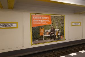 Im Berliner U-Bahnhof Kochstraße am Checkpoint Charlie hängt eine Plakatwerbung der BSR zur Stadtsauberkeit aus 2021. Auf dem Plakat sitzt ein Geschäftsmann mit seinem Smartphone auf einer Bank, neben ihm seine Bürotasche. Neben der Bank steht ein Papierkorb mit der Aufschrift "Müllkippchen". Vor ihm liegt seine überdimensional große ausgedrückte Kippe. Die Headline der Kampagne lautet: „Erst heißt gemacht, dann weggeworfen.“ Die Subline löst auf: „Zigarettenstummel schaden der Umwelt. Wirf deine Kippe bitte in den nächsten Ascher.“