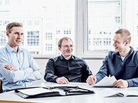 In einem Büro sitzen drei Männer vom Ico Lux Team an einem Schreibtisch.